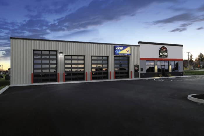 Exterior of a modern auto service center with multiple garage doors, large windows, and signage on the facade during dusk.