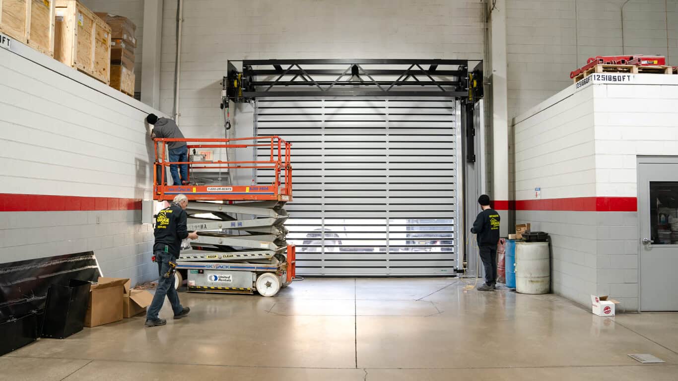 Workers install a large garage door inside an industrial building using a scissor lift.