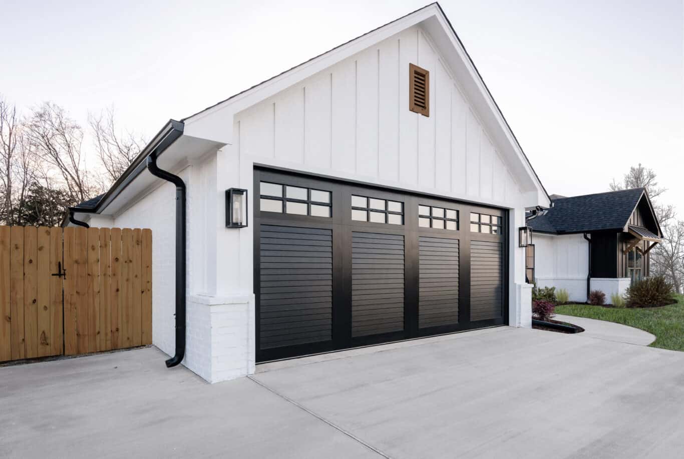 A modern white house with a black two-car garage, a fenced yard, and an attached sloped roof.