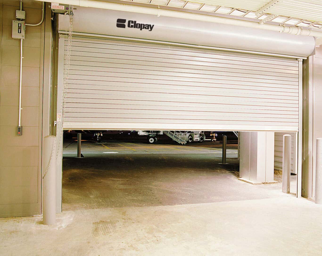 A partially opened commercial overhead door with Clopay branding offers a glimpse of the outside area.